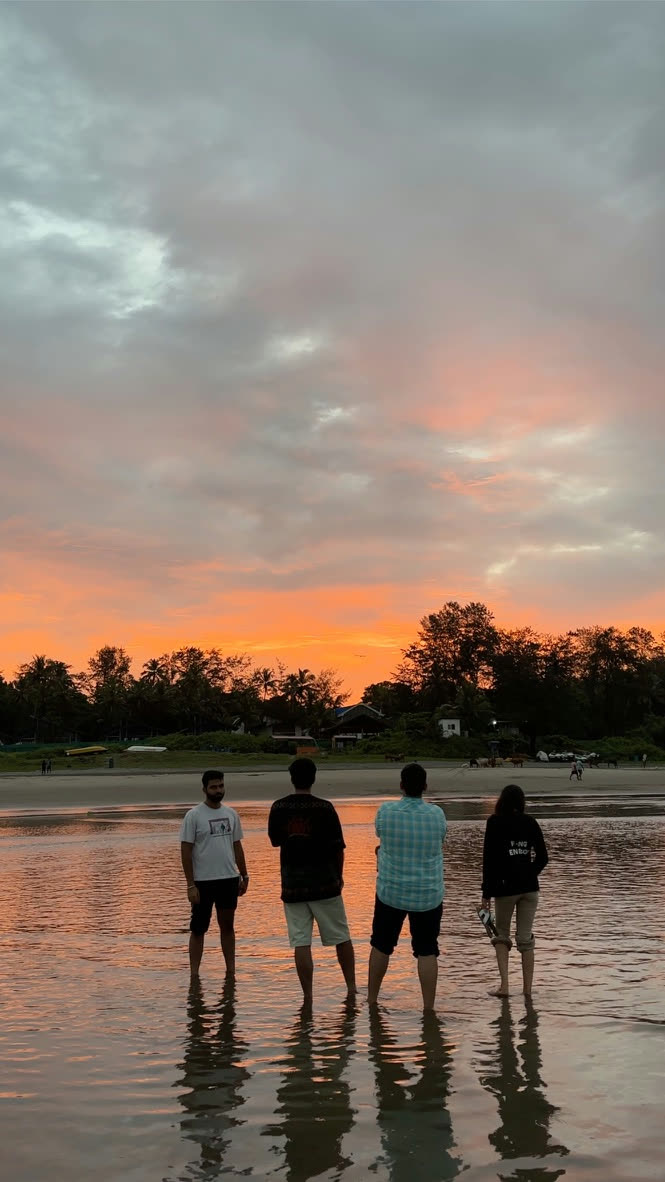 Four friends standing ankle-deep on a beach at sunset